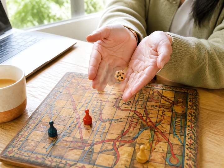 Hands releasing a wooden die over an old hand-painted Indian board with snakes and arrows, in afternoon daylight